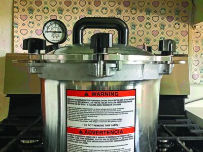 silver colored pressure canner sitting on stovetop with canning